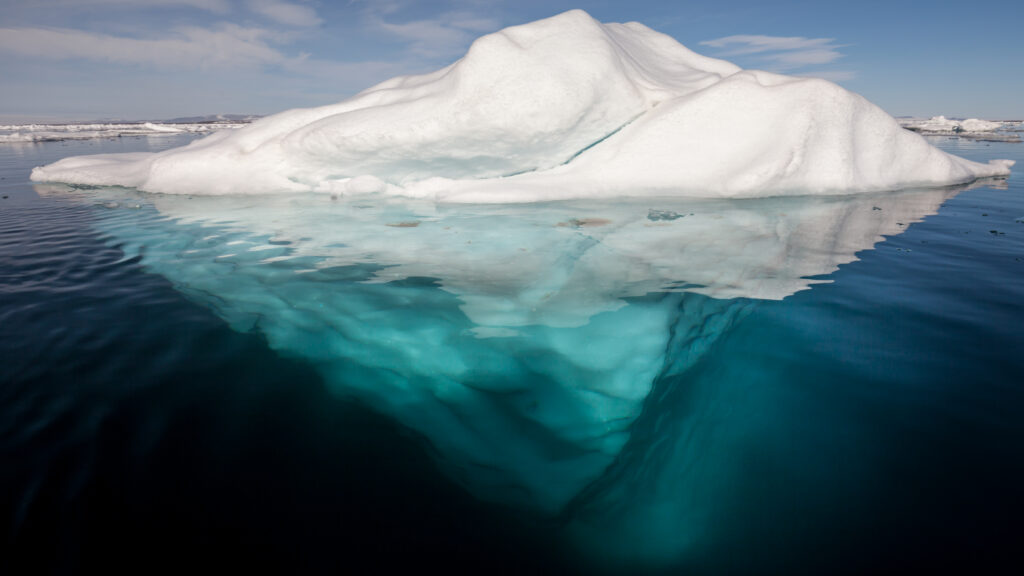 iceberg in the arctic with its underside exposed, brightened underwater